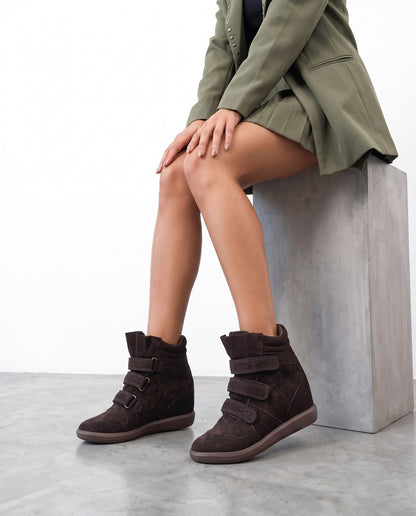Modella seduta su blocco di cemento con sneakers wedge marroni in camoscio con cinturini a strappo