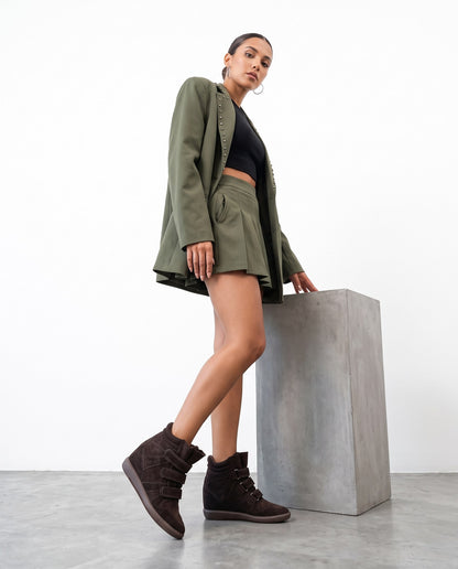 Modella in abito verde militare con sneaker alte marroni, in posa accanto a un blocco di cemento.
