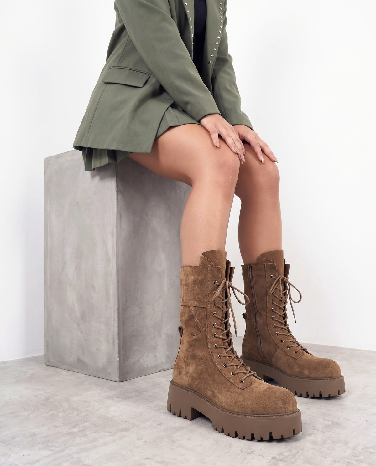 Modella seduta su blocco di cemento, stivali camoscio camel con lacci e suola carrarmato, blazer verde militare