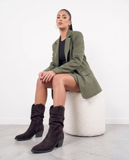 Modella seduta su pouf bianco, stivali texani camoscio marrone scuro con zip, outfit verde militare