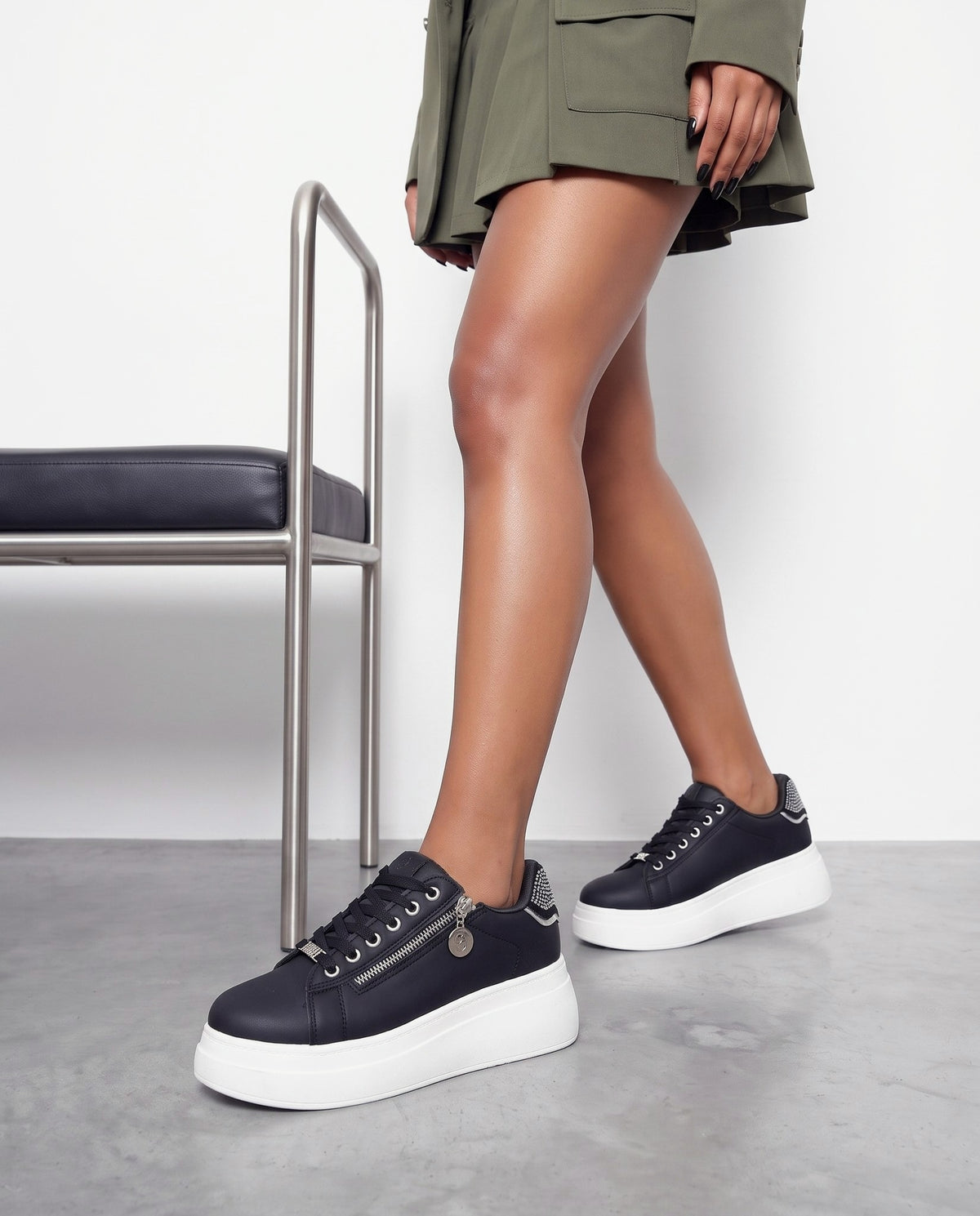 Dettaglio ravvicinato delle gambe e delle sneakers nere con suola bianca e zip laterale