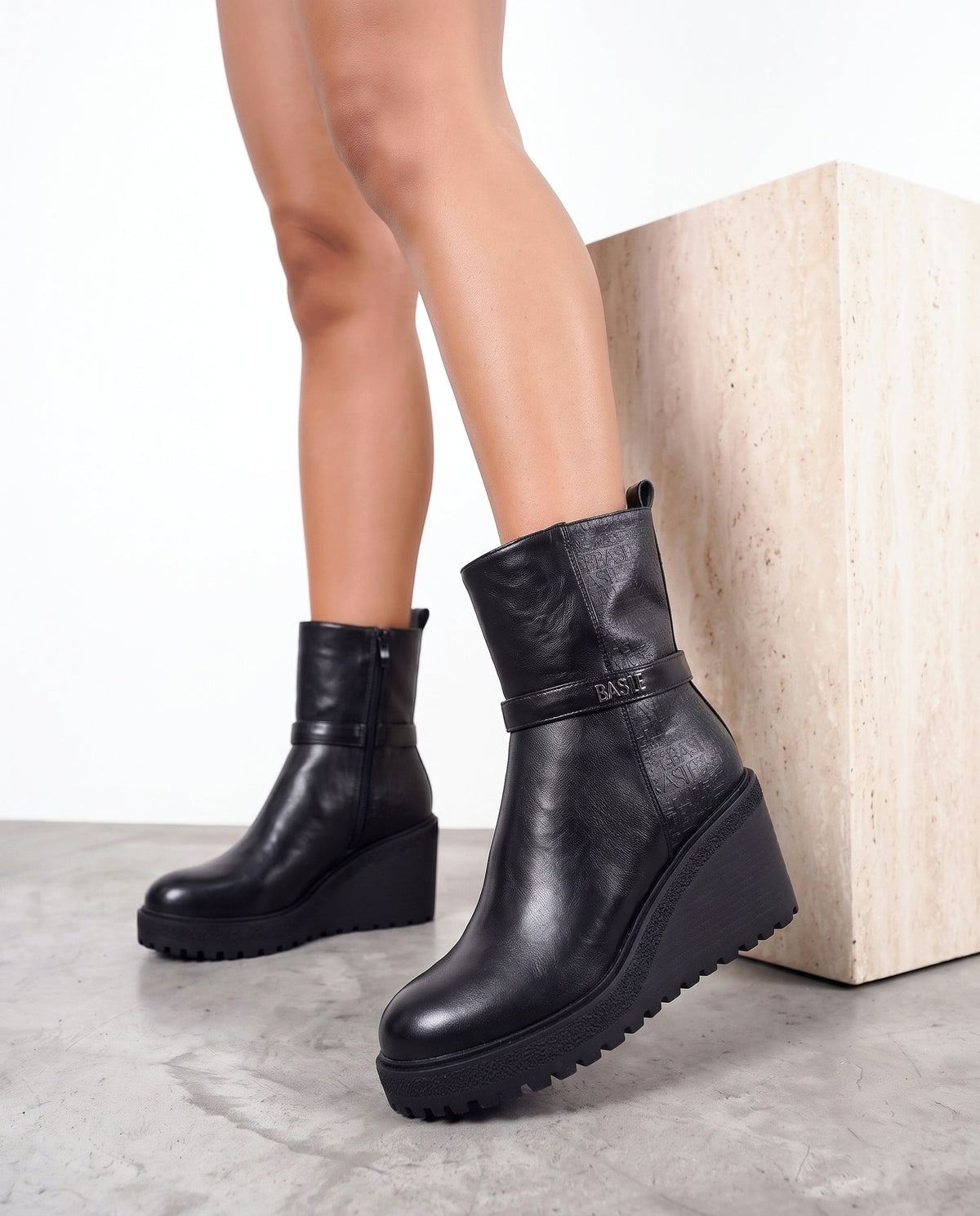 Dettaglio stivaletto nero wedge con fibbia, vicino al cubo in travertino su pavimento in cemento