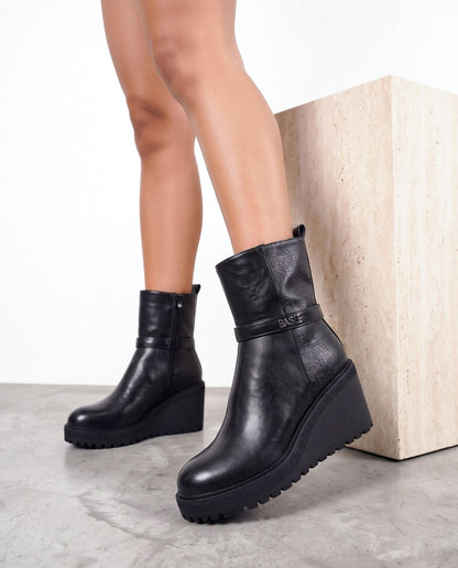 Dettaglio stivaletto nero wedge con fibbia, vicino al cubo in travertino su pavimento in cemento