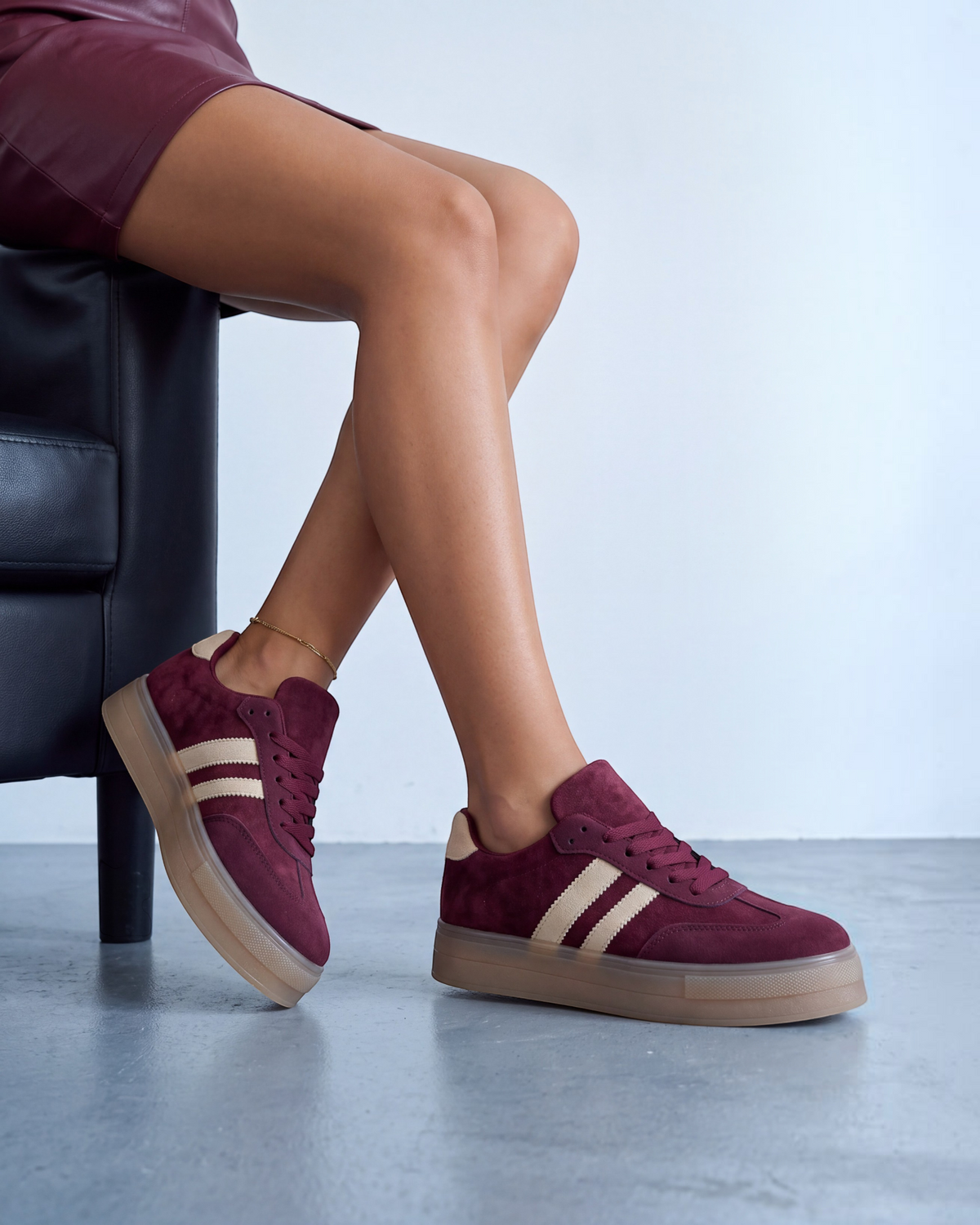 Sneakers donna in ecocamoscio bordeaux con bande beige e suola gum, indossate seduta